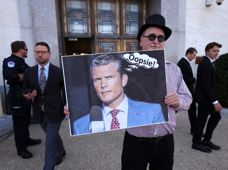 Un manifestante mantiene una foto de Pete Hegseth con una burbuja del habla que dice: "¡Oopsie!"