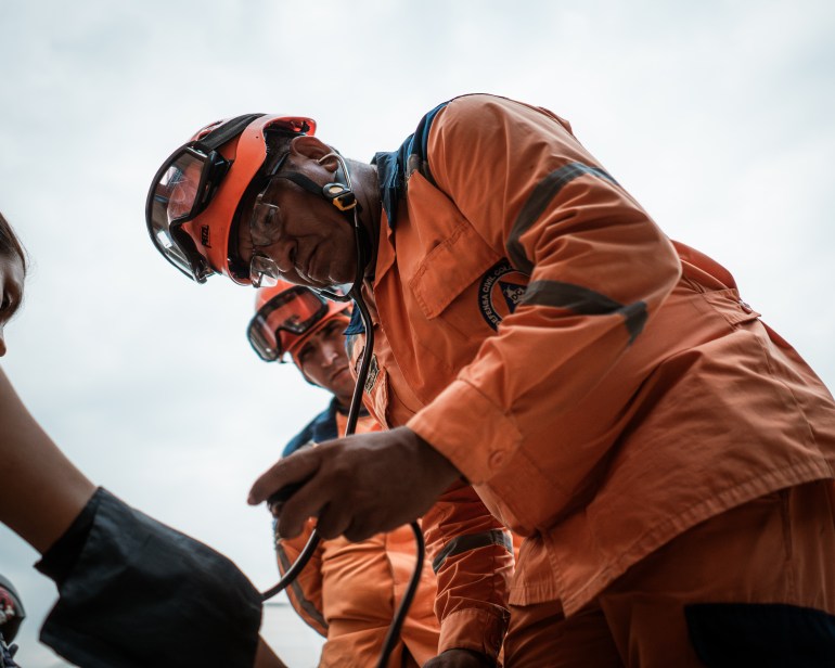 Edgar Larga - miembro de la defensa civil colombiana, vestida con uniforme y casco naranja, toma la presión arterial de una mujer recientemente llegó de Catatumbo.